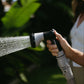 hand holding spray gun and spraying water with leaves in background