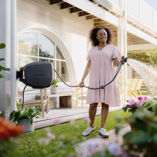 Woman in a pink dress watering a flower garden with a charcoal evolve retractable hose reel