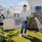 Older woman in a light blue blouse and jeans in front of a weatherboard house watering her lawn with a beige Evolve Retractable Hose Reel