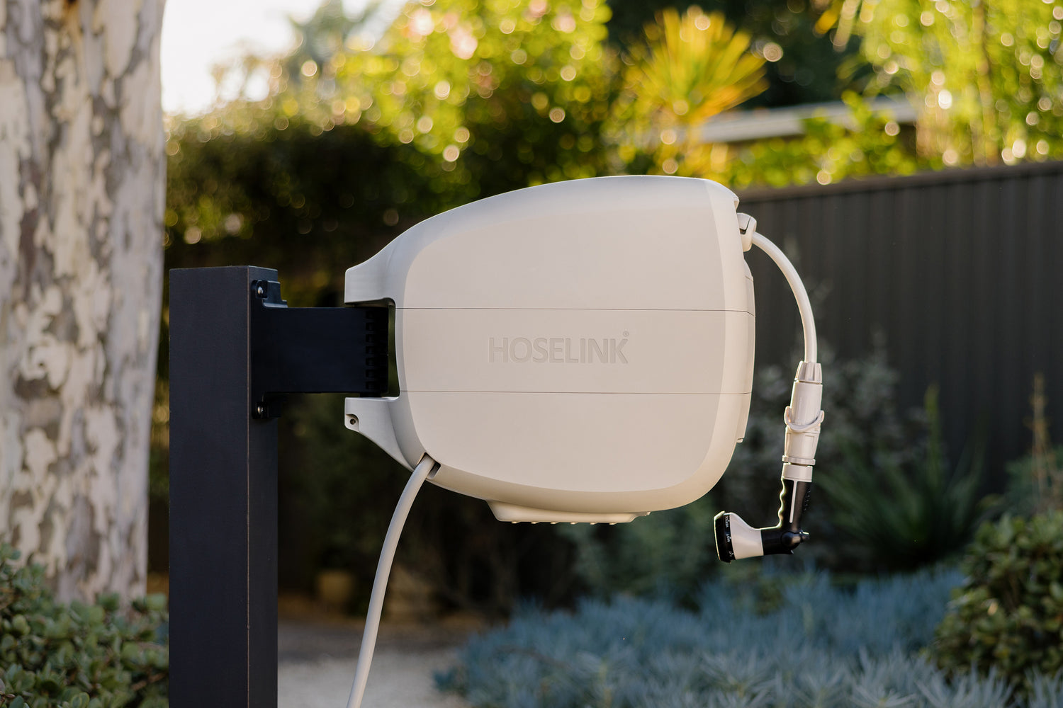 Beige Evolve Retractable Hose Reel on a black timber post with a gum tree and green succulents in the background