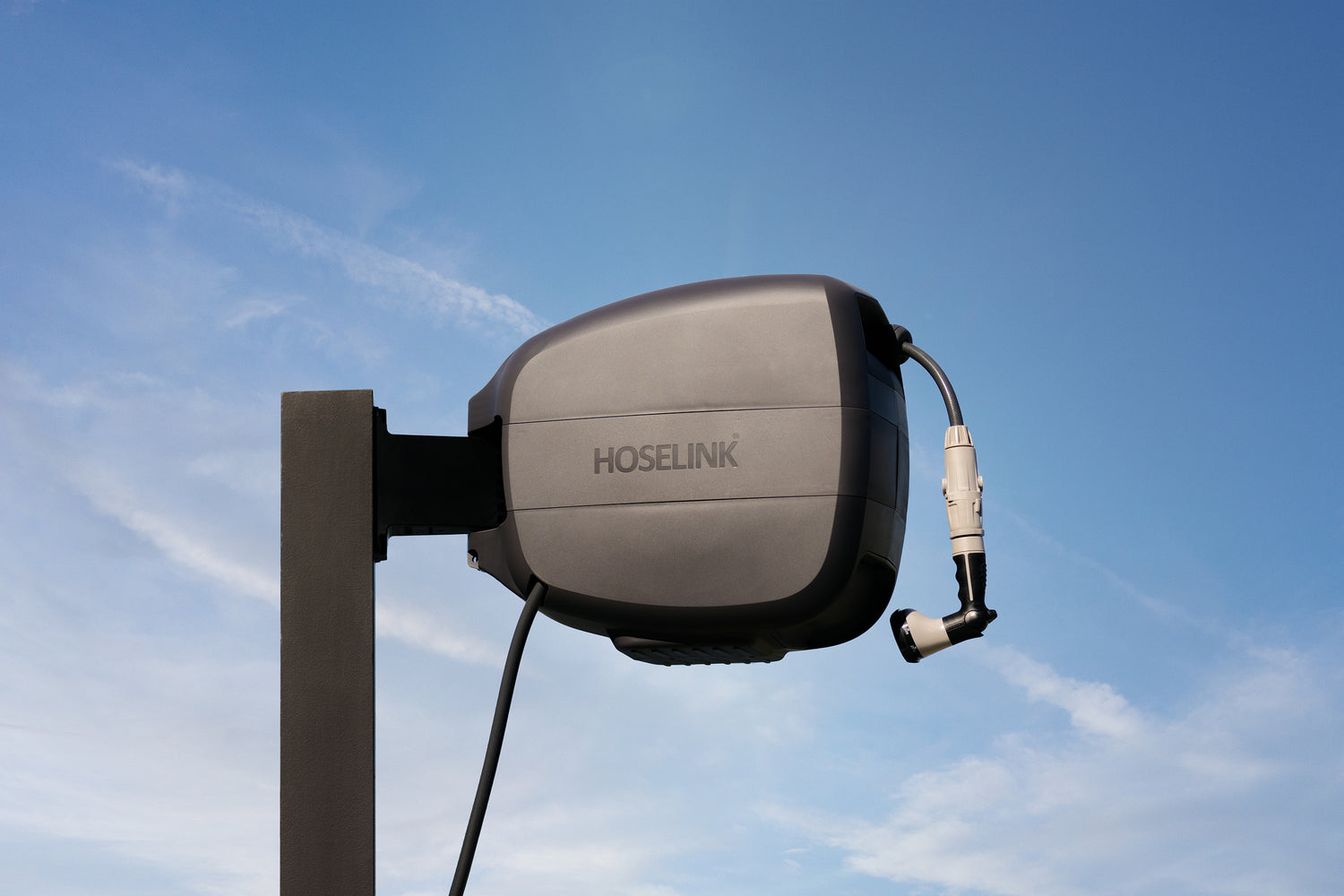 Charcoal Evolve Retractable Hose Reel mounted on a black timber post with blue sky and clouds in the background