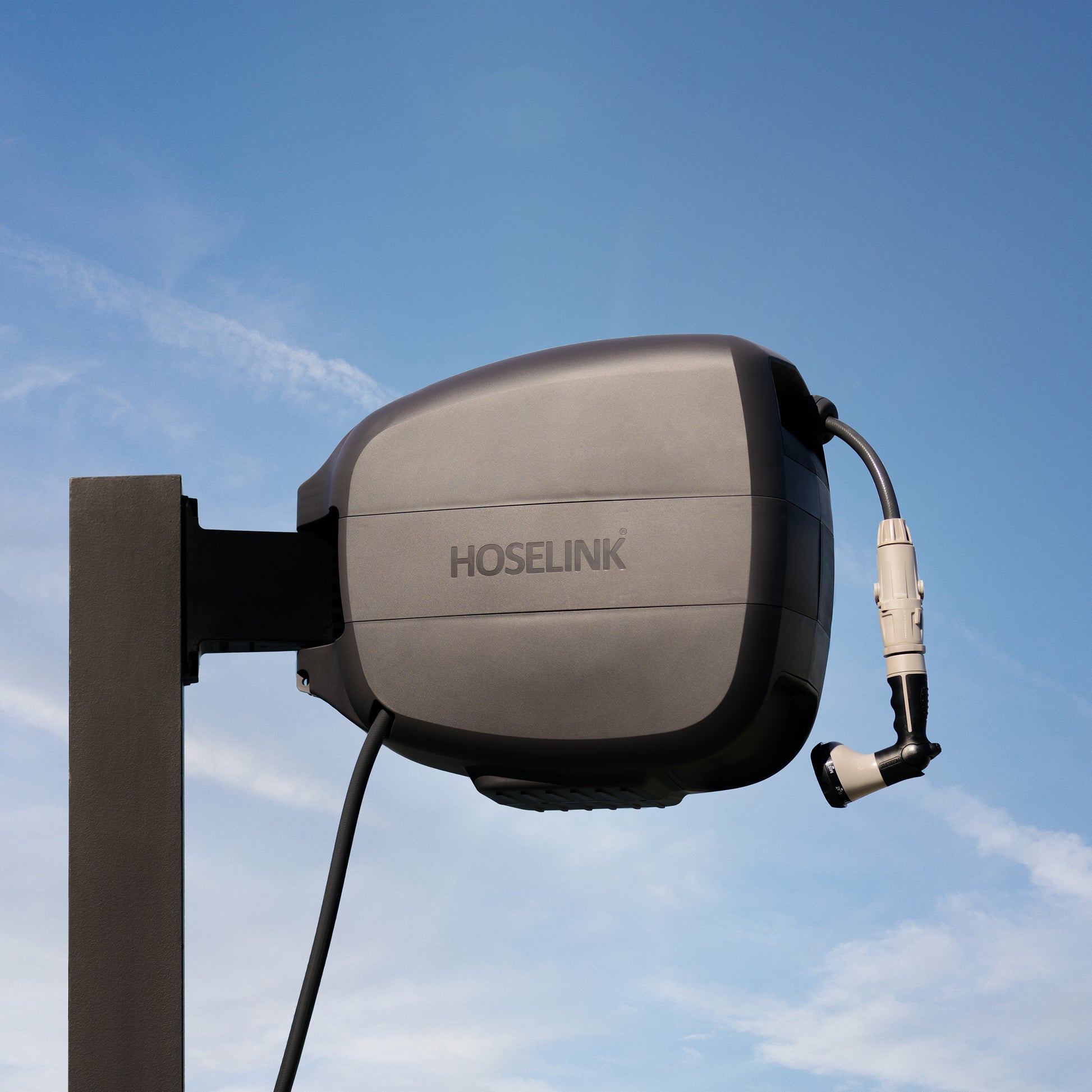 Charcoal Evolve Retractable Hose Reel mounted on a black timber post  with nothing but blue sky and clouds in the background