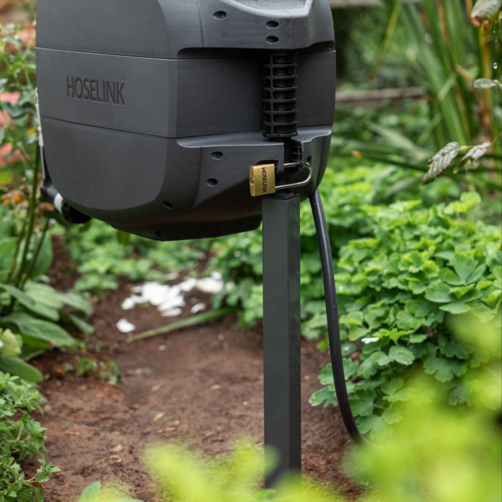 Evolve Retractable Hose Reel charcoal mounted on an Evolve series Mounting Post and secured with an Evolve Padlock in a garden bed