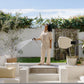 Woman standing on wooden deck in the back garden using an Evolve Beige Retractable Hose Reel to water an olive tree