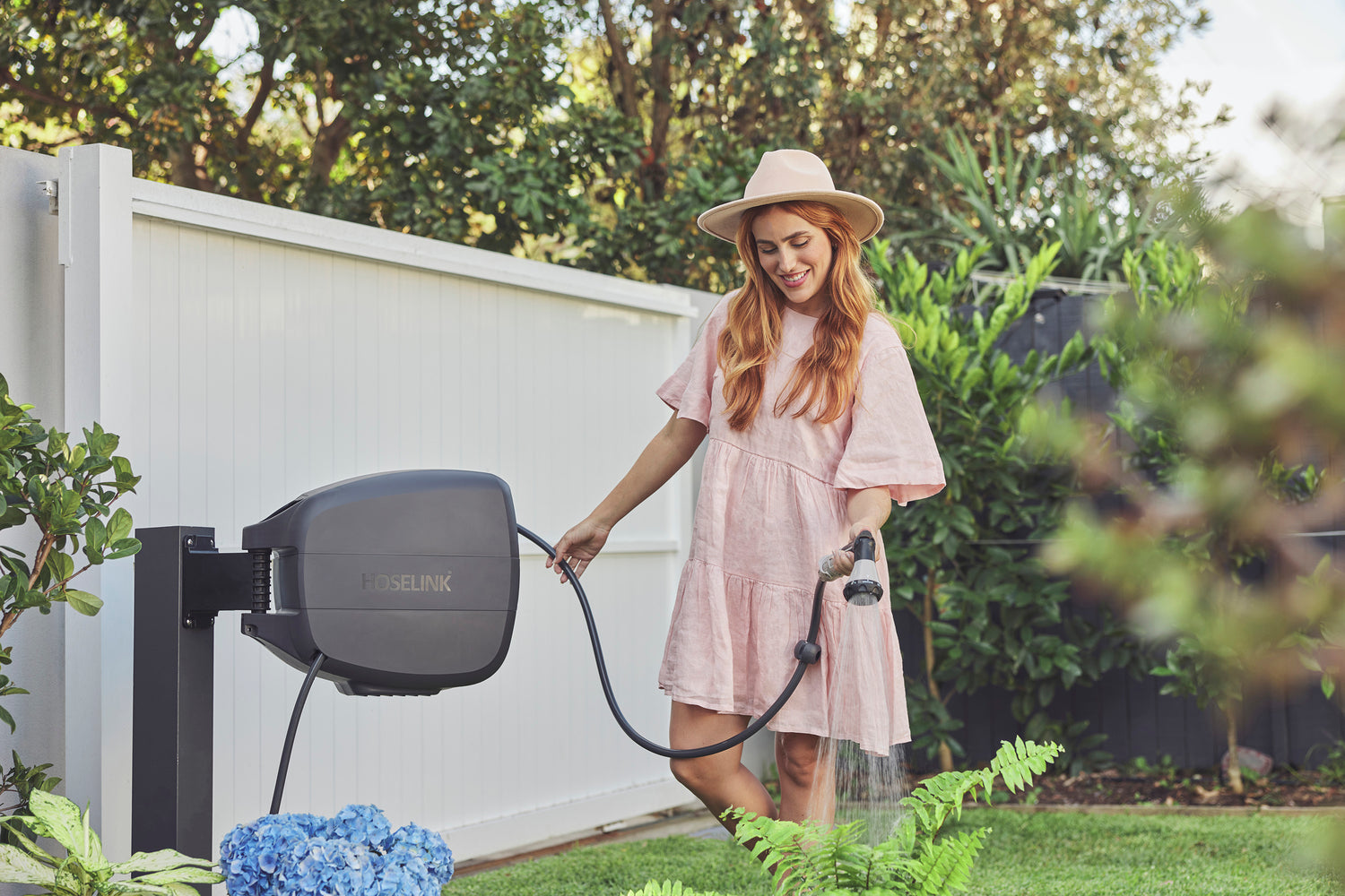 Female wearing a pink dress and hat watering her garden with the Charcoal-colour Evolve Retractable Hose Reel