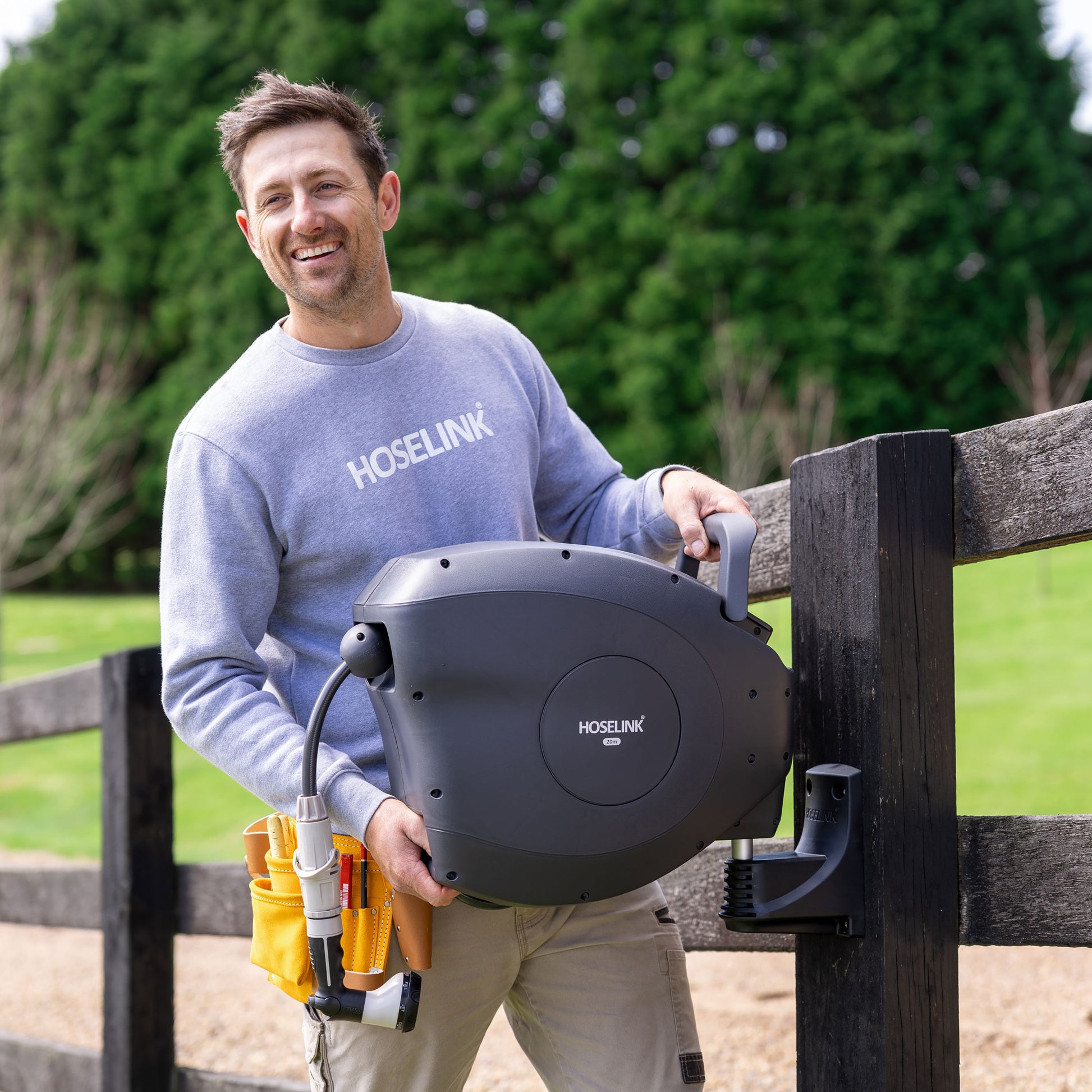 Ben Hayman installing a charcoal classic hose reel on a black wooden post next to a gravel road