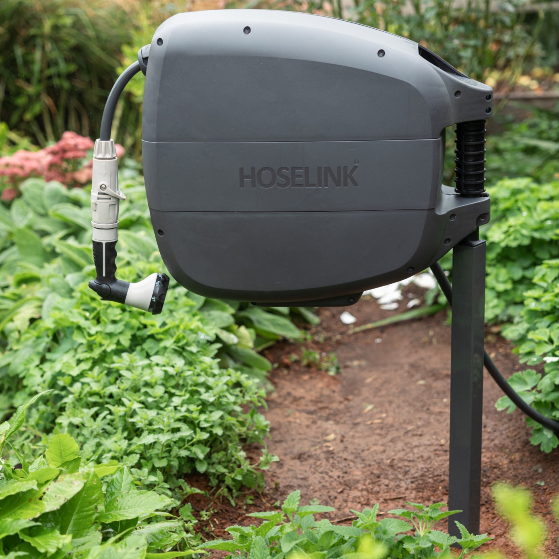 Charcoal Evolve Retractable hose Reel mounted on an Evolve Series mounting post in a garden surrounded by lush green foliage 