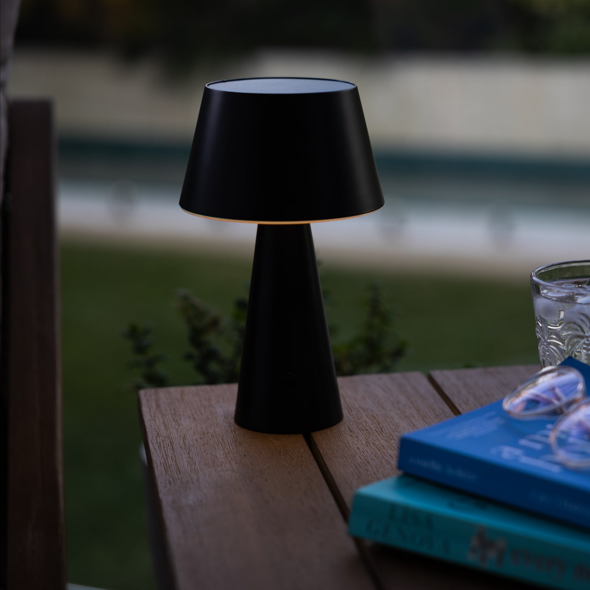 black table lantern on the corner of an outdoor wooden table next to a glass of water