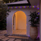 Multicoloured solar rope lights strung around a house and archway at dusk