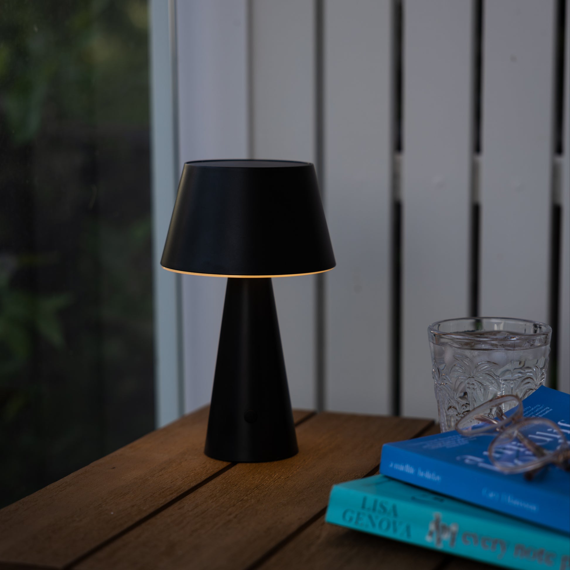 black table lantern on the corner of an outdoor wooden table next pair of blue books