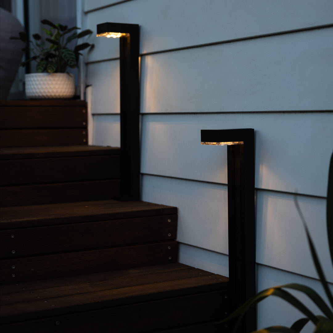 Two solar path lights on wooden steps in front of a white weatherboard house