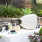 Evolve Beige Retractable Hose Reel sitting next to a Fertiliser Spray Mixer, Adapter Pack, 9-pattern Sprinkler and Seaweed Tonic on a white stone bench in front of a garden bed