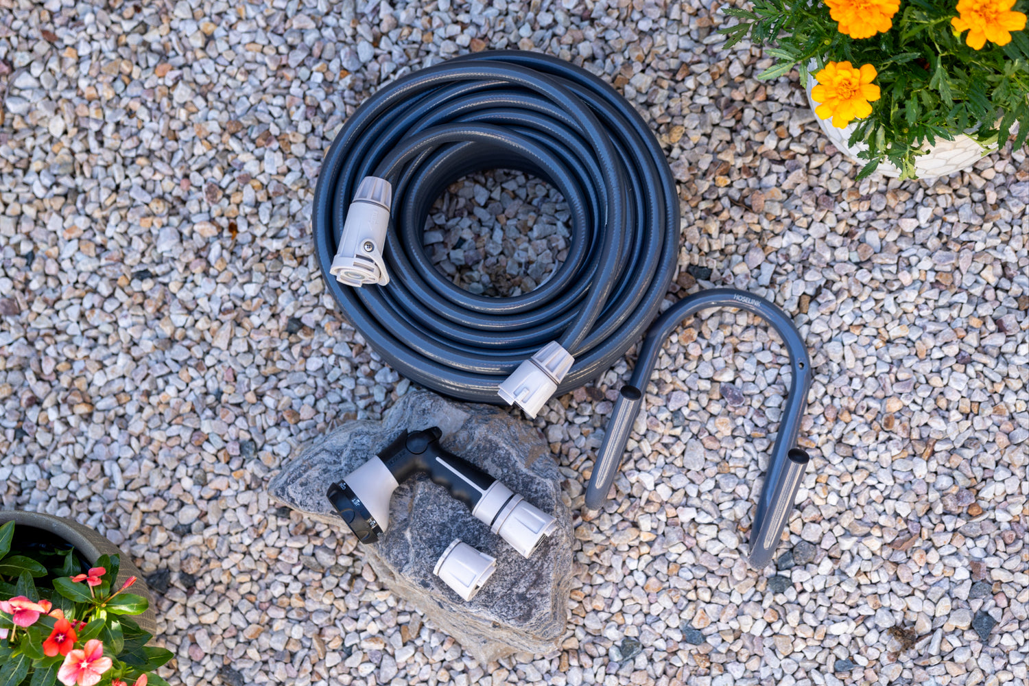 charcoal hose and hanger, warm grey spray gun sitting on white gravel and a rock with flowers in the corner