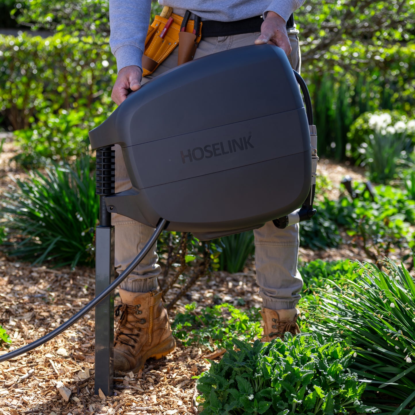 Tradesman placing a charcoal Evolve retractable hose Reel on a mounting post they have installed in a garden