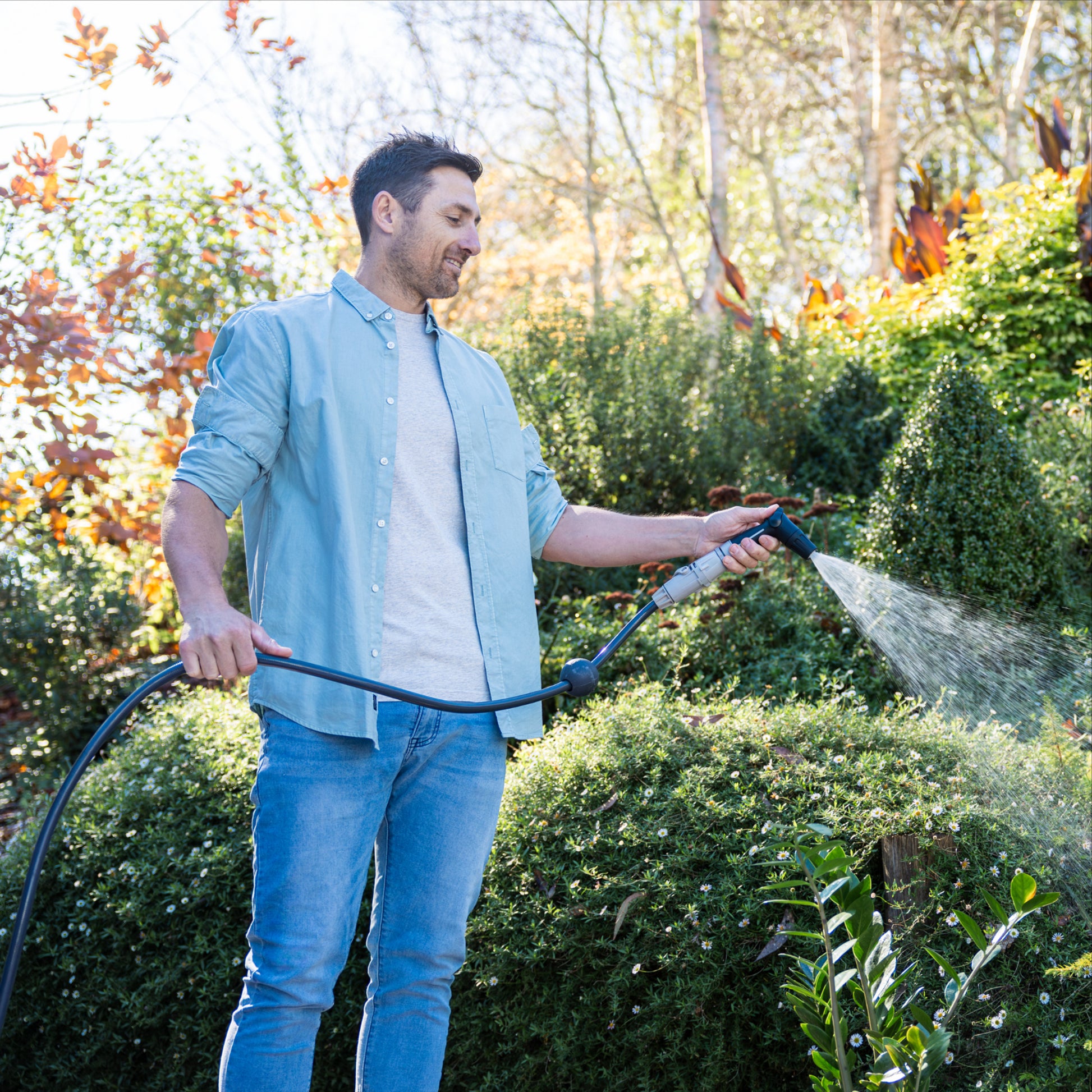 Ben Hayman in jeans and a blue shirt watering hedges with the compact flow control spray nozzle