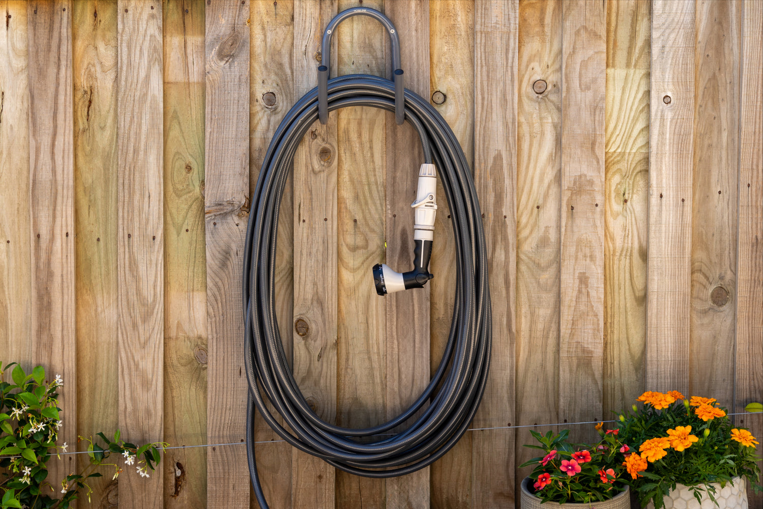 Charcoal hose, hanging on a charcoal hanger mounted to a wooden fence with flowers at the base