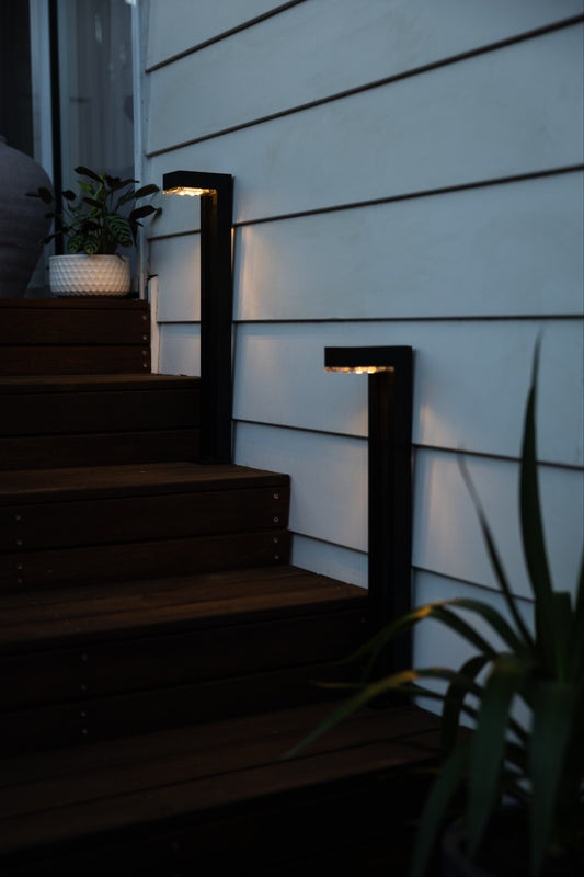 Two solar path lights on wooden steps in front of a white weatherboard house