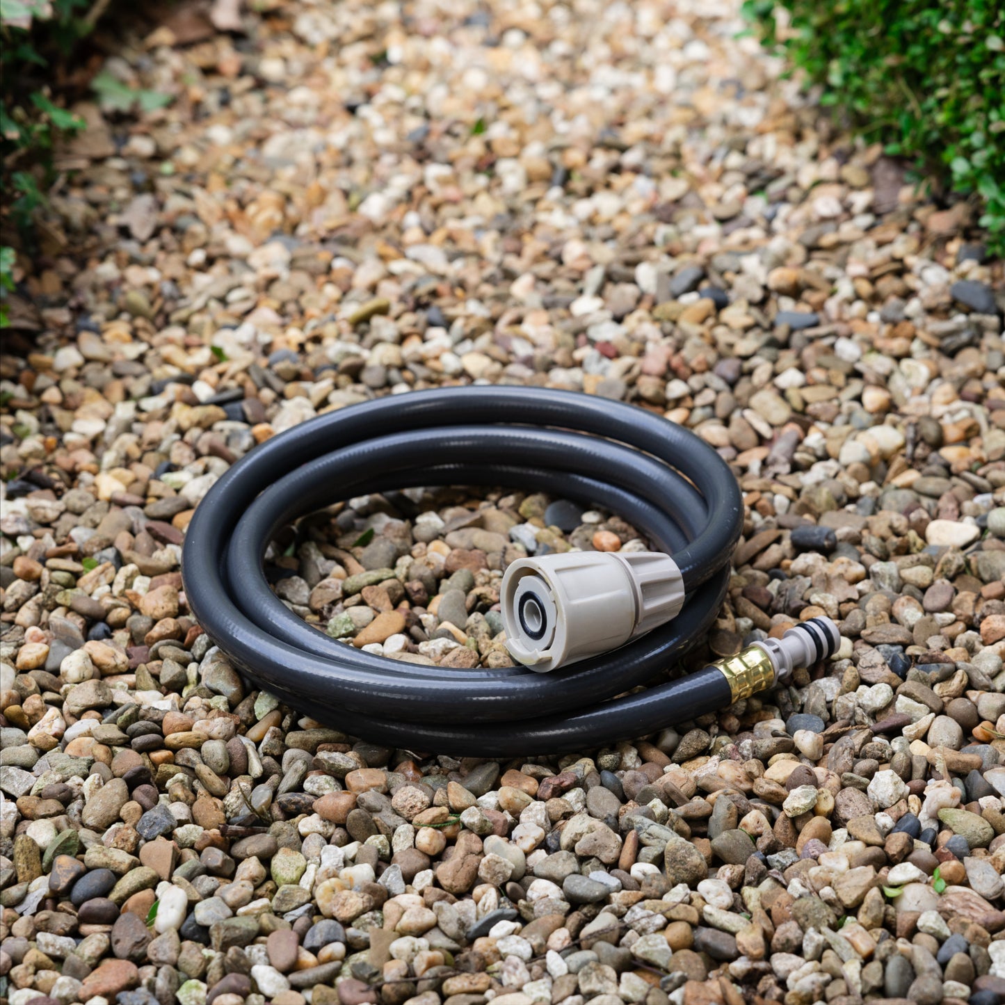 Coiled charcoal replacement leader hose sitting on a brown gravel path