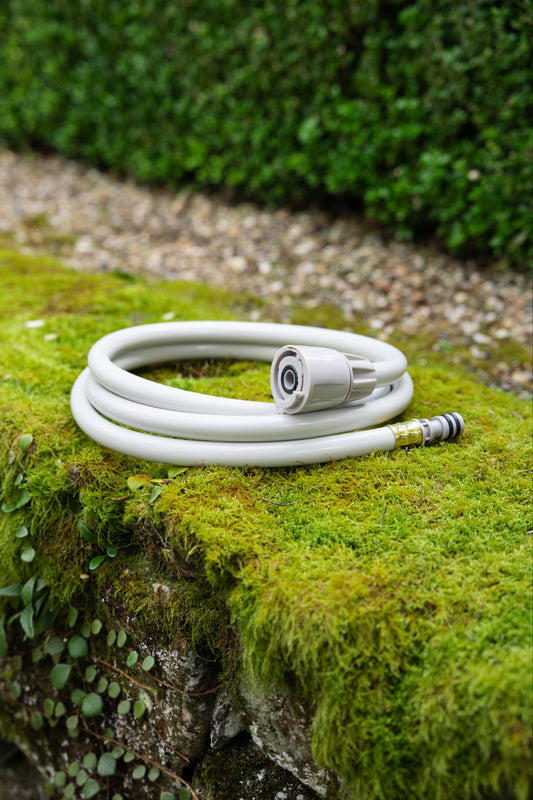 Coiled beige replacement leader hose sitting on a green moss covered stone wall